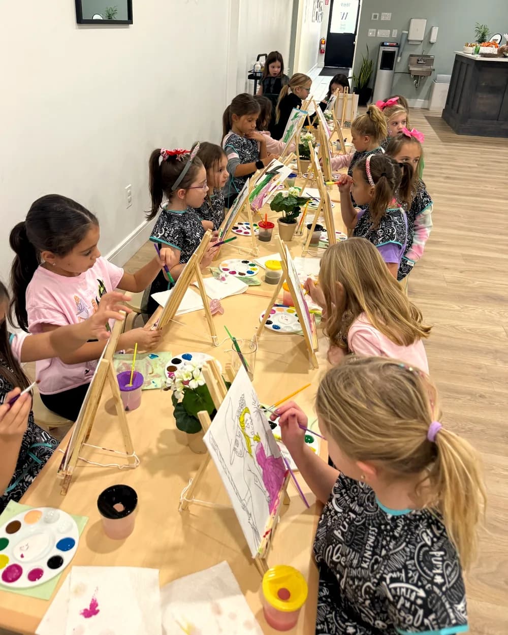 Kids painting at easels along a long table during an art party at Workshop