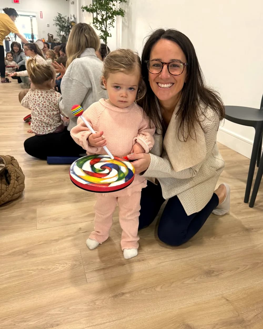 A toddler holding a rainbow lollipop prop with a Workshop instructor at a music class